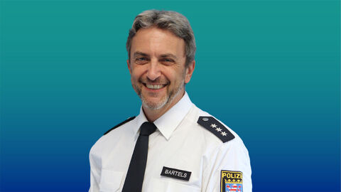 Polizeibeamter mit grauen Haaren und Bart im weißen Diensthemd mit Krawatte