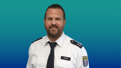 Polizeibeamter mit kurzen dunklen Haaren und Bart im weißen Diensthemd mit Krawatte