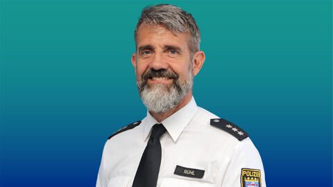 Polizeibeamter mit grauen Haaren und Bart im weißen Diensthemd mit Krawatte