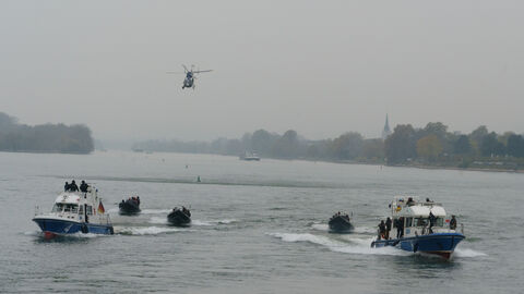 Zwei große Streifenbott und drei Schlauchboote auf dem Rhein, darüber der Polizeihubschrauber