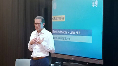 Martin Hofmockel; Leiter Fachbereich Jugend und Familie des Werra-Meißner-Kreises; Herr Hofmockel steht mit einem Mikrofon in der Hand in Blickrichtung Publikum, im Hintergrund eine Präsentationswand