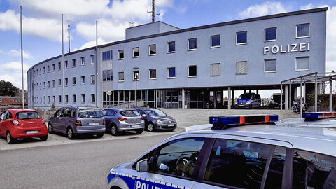 Polizeirevier Mitte in Kassel; Foto zeigt das Liegenschaftsgebäude des Polizeireviers mit der Zufahrt bei blauem Himmel, im Vordergrund stehen Autos und ein Streifenwagen