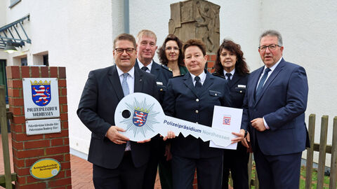 Neue Leitung der Polizeistation Homberg; Foto zeigt mehrere zusammen stehende Personen vor dem Eingang zur Polizeistation in Homberg, im Vordergrund überreicht PP Bärtl einen symbolischen Schlüssel mit Polizeistern und Schriftzug Polizeipräsidium Nordhessen (ca. 80 cm groß) an Silke Pollack
