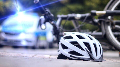 Ein Fahrradhelm liegt vor einem umgestürzten Fahrrad auf der Straße, daneben ist ein Polizeifahrzeug mit eingeschaltetem Blaulicht