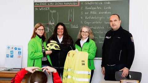 Übergabe der neuen Helme und Startnummern an den Verkehrserziehungsdienst in Nordhessen; v.l.: Frau Anacker, Frau Angersbach, Frau Lohrmann und Herr Weiser bei der Übergabe in einem Klassenraum vor der Wandtafel stehend mit Blick in Richtung Schulkinder