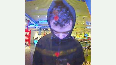 Foto des unbekannten Täters: Männlicher Täter mit Kaputzenpullover und dunklen kurzen Haaren steht mit Blick in Richtung der Kamera eines Geldautomaten
