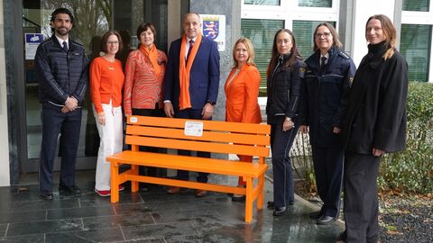 Verschiedene Vertreterinnen und Vertreter des Polizeipräsidiums Westhessen und von Zonta Wiesbaden an der orangen Bank vor dem Polizeipräsidium Westhessen