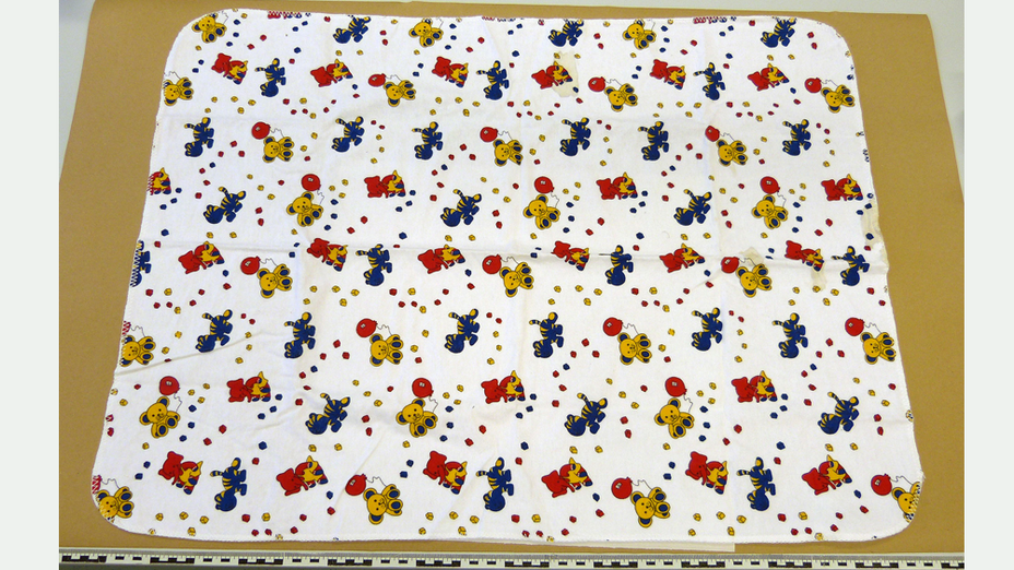 Weisse Babydecke mit vielen gelben Teddybären mit roten Luftballons, blau-gelbe Katzen und roten Elefanten mit gelbem Tuch, dazwischen jeweils rote, blaue und gelbe kleine Würfel