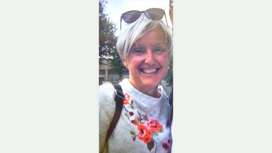 53-jährige Frau mit sehr hellen Haaren, Sonnenbrille im Haar und hellem Pullover mit Blumenmuster